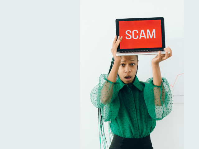 SCAM(詐欺)と表示されたPCを掲げる女性